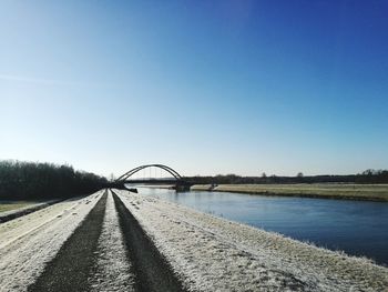 Road by river against clear blue sky