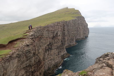 People on rock by sea against sky