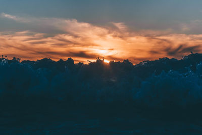 Silhouette landscape against dramatic sky during sunset