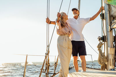 Low angel view of couple standing on sailboat against sea