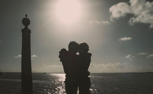Silhouette couple standing by sea against sky