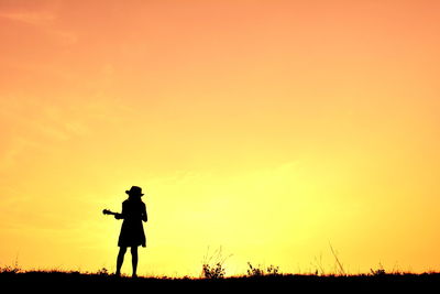 Silhouette of woman playing ukelele at sunset