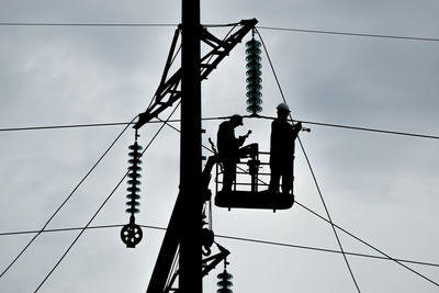Low angle view of workers working on electricity pylon against sky