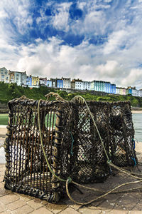 Wet lobster trap on footpath by harbor against cloudy sky