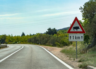 Road sign by trees against sky