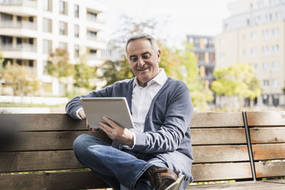 Smiling senior man using tablet pc sitting on bench