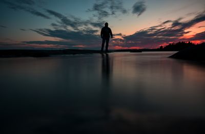 Silhouette man standing by lake against sky during sunset