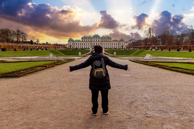 Young girl with arms outstretched in front of schloss belvedere in vienna. 