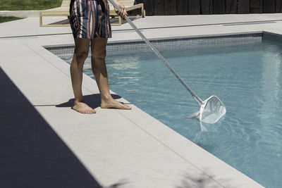 Unrecognizable man cleaning the swimming pool manually with white cleaning net at his house outdoors