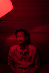 Portrait of young man standing against red wall