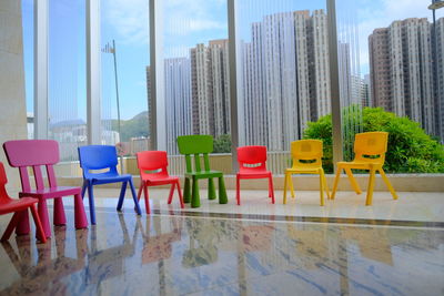 Empty chairs and tables by swimming pool against buildings in city