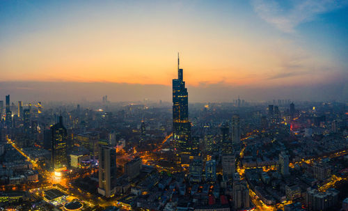 Illuminated buildings in city against sky during sunset