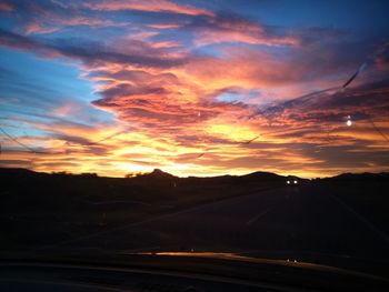 Scenic view of landscape against cloudy sky at sunset