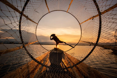 Silhouette man standing by fishing net against sky during sunset