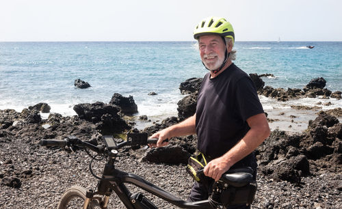 Portrait of smiling senior man with bicycle against sea and sky during sunny day