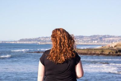 Rear view of woman standing by sea against clear sky