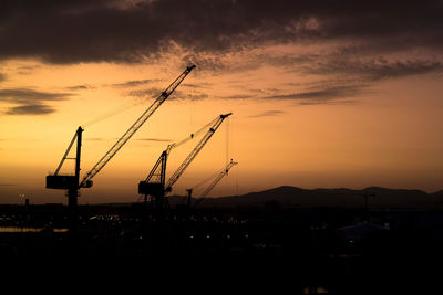 Silhouette cranes against sky during sunset