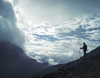 Silhouette of man standing on mountain against cloudy sky