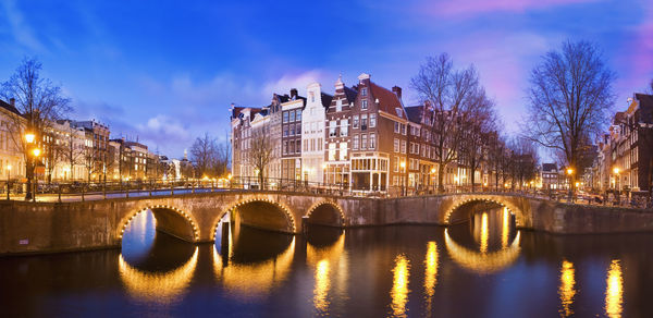 Bridge over river by buildings against sky