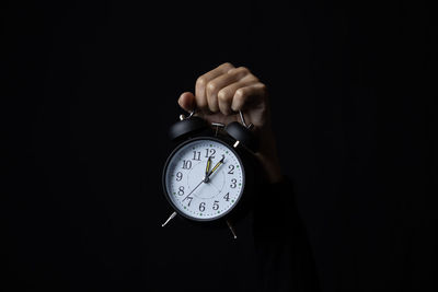 Close-up of hand holding clock over black background