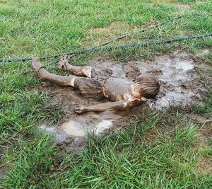 High angle view of playful muddy boy lying on grassy field