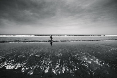 Mid distance view of woman standing at beach against cloudy sky