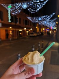 Midsection of person holding ice cream in illuminated city at night