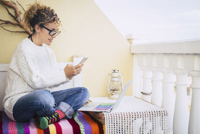 Young woman using phone while sitting on laptop