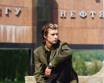 Young man looking away while sitting outdoors