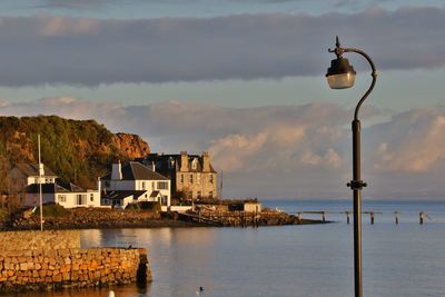 Illuminated street light by sea against sky