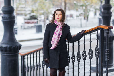 Portrait of young woman standing against railing