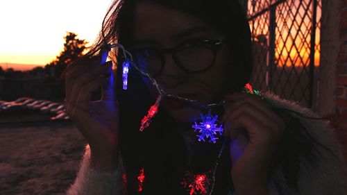 Close-up of woman with illuminated flowers against sky at night