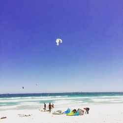 Kiteboarders at beach against clear sky