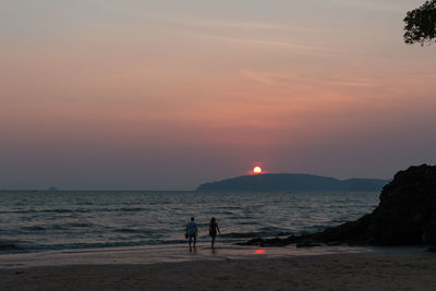 Two people walking on beach at sunset