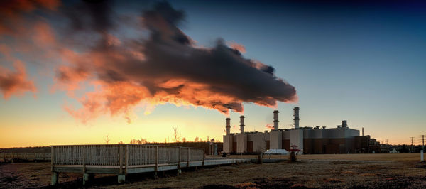 Smoke emitting from factory against clear sky at sunset