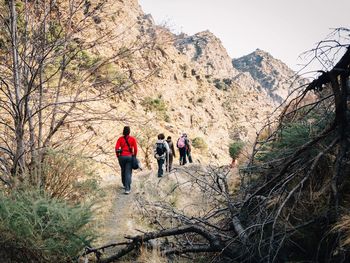 Rear view of people walking on footpath against rocky mountains