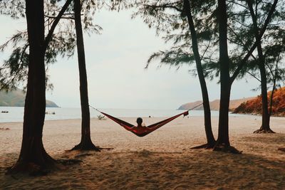 Woman relaxing in hammock at beach against sky