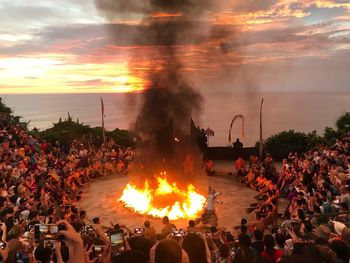 Group of people on bonfire against sky during sunset