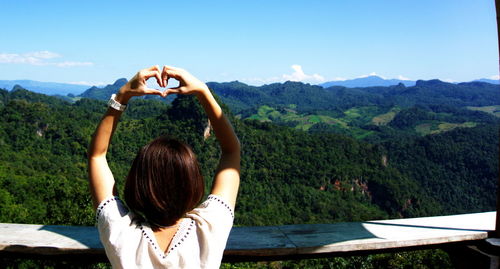 Rear view of woman making heart shape against mountains