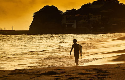 Silhouette man standing on beach against sky during sunset