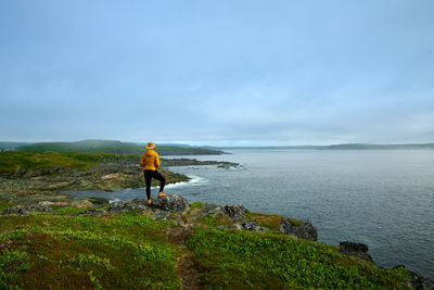 Rear view of woman standing at beach against sky
