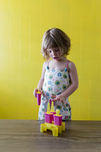 Cute girl playing with toys on table against yellow wall