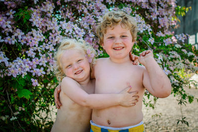 Portrait of smiling siblings embracing against plants