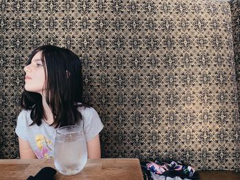 Young woman sitting on table against wall