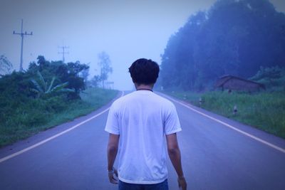 Rear view of man standing on road against trees