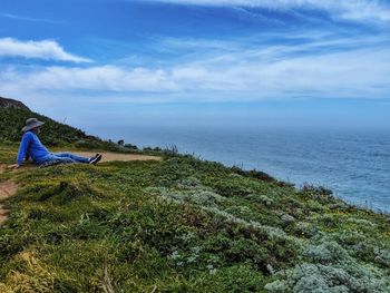 Side view of man looking at sea against sky while sitting on mountain