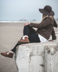 Side view of woman sitting on railing at beach