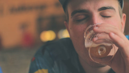 Close-up of young man with eyes closed drinking beer in glass