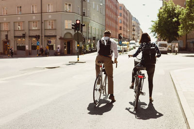 Rear view of business colleagues riding bicycle on city street