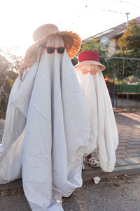 Trendy sheet ghosts costumes on little kids standing on a suburbs street. happy halloween holiday